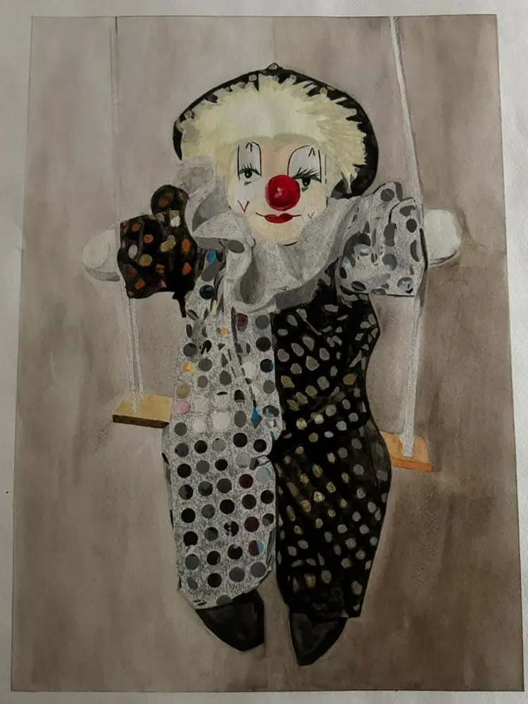 Clown on a Swing: a clown doll in a polka-dot suit sits on a swing, half white and half black, with a red nose and a frilled collar